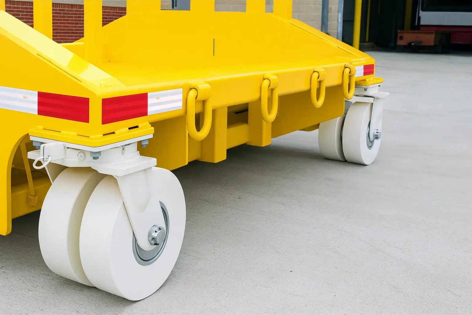 Yellow steel coil cart with dual white MC Nylon caster wheels on a smooth concrete floor