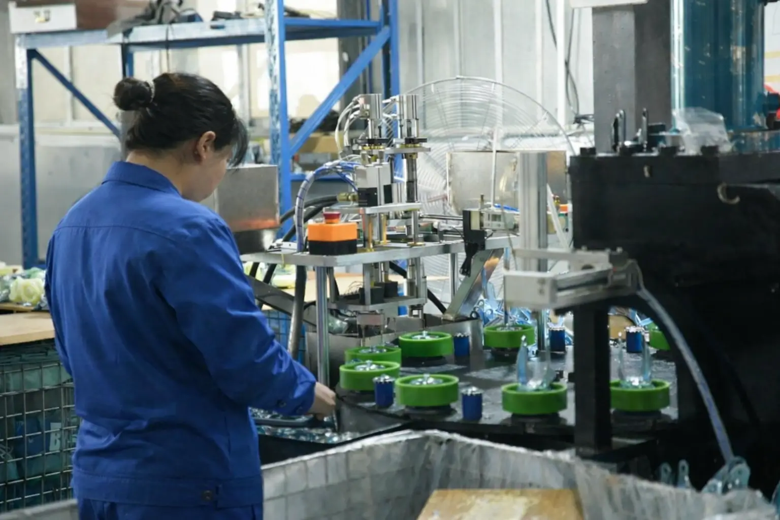 Factory worker operating an automated machine assembling caster brackets on a production line.