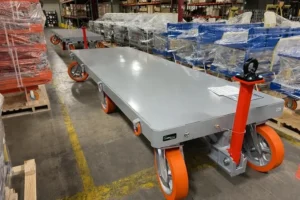 Heavy-duty flatbed carts with bright orange polyurethane wheels lined up in a warehouse for material handling.