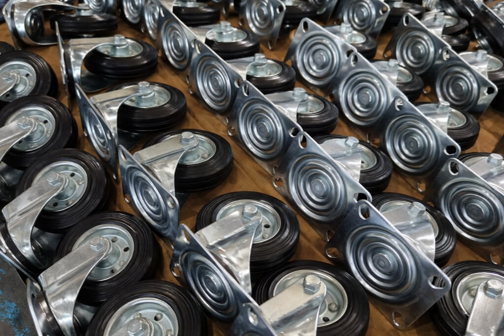 Rows of industrial caster wheels with black rubber tires and galvanized metal brackets, neatly arranged on a flat surface