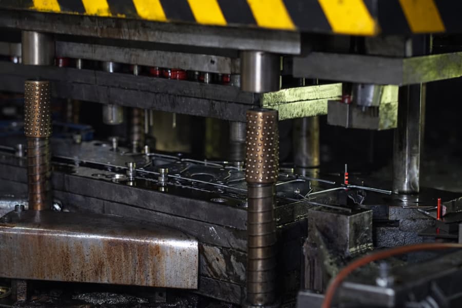 Industrial metal stamping machine pressing sheet metal parts inside a factory, with heavy steel tooling and mechanical components forming metal pieces